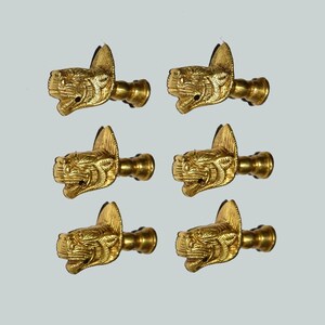 以下が含まれることがあります： 金色の金属製引き出しノブ6個セット。それぞれに詳細な立体的な虎の頭のデザインが施されており、取り付け用の円筒形のポストが背面に付いています。3つずつ2列の縦並びで配置されています。