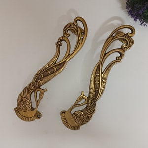 Puede incluir: Dos tiradores de puerta de latón adornados con forma de pavo real con detalles intrincados. Los tiradores son de color dorado y tienen un diseño decorativo.