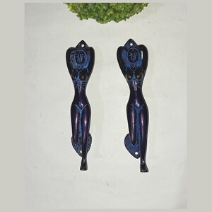 Puede incluir: Dos tiradores de puerta decorativos con forma de figura femenina. Los tiradores están hechos de latón y tienen un acabado azul oscuro con detalles en azul claro.