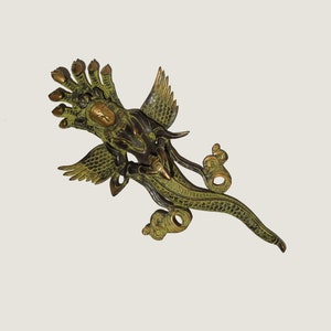 Könnte beinhalten: Eine grüne und goldene Metallskulptur einer mythischen Kreatur mit einem menschlichen Gesicht und einem Schlangenleib. Die Kreatur hat Flügel und mehrere Arme.