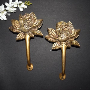 May include: Two gold-toned metal door handles shaped like lotus flowers. The handles have a detailed design and are attached to a long, thin stem.