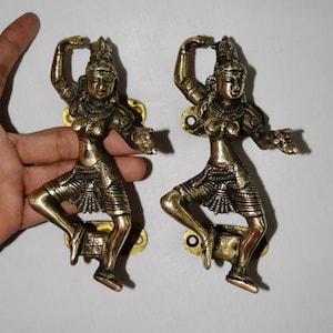 May include: Two gold-toned metal door handles shaped like dancing figures. The figures are in a traditional Indian style, with elaborate jewelry and flowing garments.