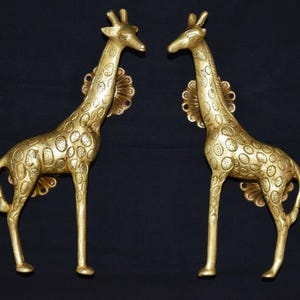 以下が含まれることがあります： 詳細な斑点模様が施された、金色のキリンの彫刻が2つ。各キリンは長い首を持ち、装飾的な裏板に取り付けられ、直立しています。彫刻は暗い背景に配置され、その複雑なデザインを際立たせています。
