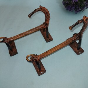 May include: Two ornate metal towel bars with horse head finials. The bars are a dark brown color with gold accents. The horse heads are facing opposite directions.