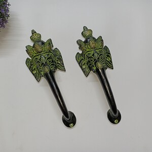 Op de afbeelding: Twee deurklinken in antieke stijl met een olifantenkopontwerp. De handgrepen zijn zwart met groene en gouden accenten, met ingewikkelde details op het gezicht en de kroon van de olifant. De handgrepen zijn van metaal.