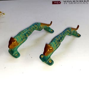 以下が含まれることがあります： 2つの虎の形をした装飾的なドアハンドル。ハンドルは、虎の頭と尾に金のアクセントが付いたターコイズ色です。金属製で、ヴィンテージ感があります。