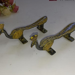 Może przedstawiać: Dwa uchwyty do drzwi w kształcie pawia z misternymi detalami. Uchwyty są wykonane z mosiądzu i mają czarne i złote wykończenie.