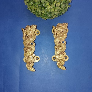 May include: Two gold-toned door handles with a detailed dragon design. The handles are made of metal and have a traditional Asian style.