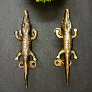 May include: Two gold-toned alligator-shaped door handles. The handles are detailed with textured scales and have a realistic alligator design.