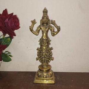 May include: A golden-colored statue of a deity with multiple arms, standing on a decorative base. The statue has intricate details and is adorned with a crown. The statue is approximately 10 inches tall.