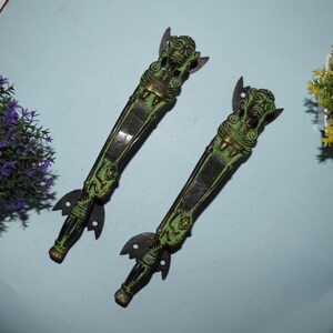 May include: Two antique brass door handles with green patina and intricate carvings. The handles feature a human figure design with a small child figure on each handle.