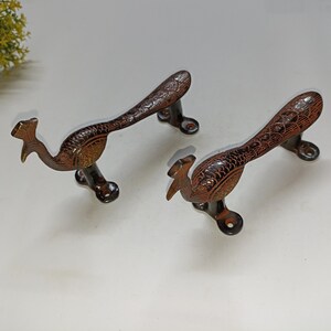 Könnte beinhalten: Zwei verzierte Türgriffe in Form eines Pfaus aus Messing mit einer dunkelbraunen Oberfläche. Die Griffe sind mit komplizierten Details gestaltet und haben einen traditionellen Stil.