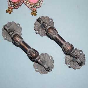 May include: Two ornate brass door handles with a floral design. The handles are a dark brown color and have a textured finish.