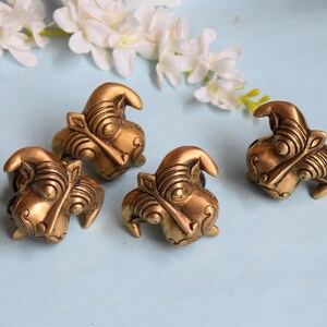 May include: Four gold-coloured metal decorative door knobs with intricate designs resembling animal faces.