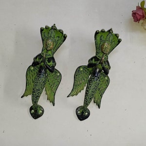 Può includere: Due maniglie per porte in metallo verde a forma di creatura mitologica con ali e coda di serpente. La creatura tiene le mani giunte in posizione di preghiera.