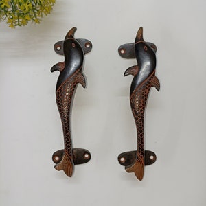 Op de afbeelding: Twee decoratieve deurgrepen in de vorm van dolfijnen. De handgrepen zijn donkerbruin met een roodbruin schubbenpatroon en een bronzen staart. Elke handgreep heeft een montageplaat met twee gaten voor schroeven.