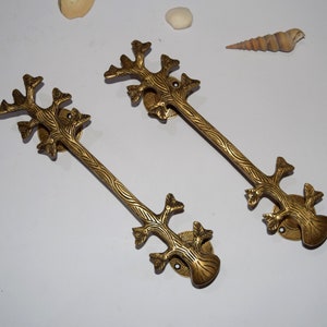 May include: Two gold-toned metal door pulls shaped like stylized trees with intricate details. The pulls are about 10 inches long and have a smooth, polished finish.
