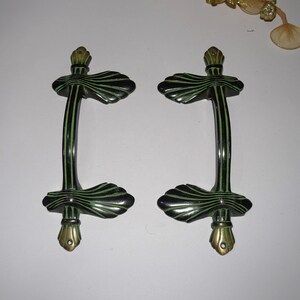 May include: A pair of decorative door handles. Each handle is black with green detailing and a curved design. The handles have a vertical grip and decorative base and top. The handles are metal and have a vintage appearance.
