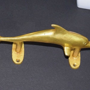 Könnte beinhalten: Ein goldfarbener Delfin-Türgriff mit zwei ovalen Montageplatten.