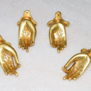 May include: Four gold-colored metal door handles shaped like hands in a prayer position. Each handle has a diamond-shaped design in the center of the palm.