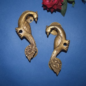 Puede incluir: Dos tiradores de puerta de latón adornados con forma de pavo real con detalles intrincados. Los tiradores son de color dorado y tienen un diseño tradicional indio.