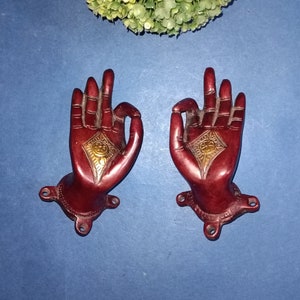Puede incluir: Dos tiradores de puerta de metal rojo en forma de mano con detalles dorados. Las manos están en un gesto de bendición o de dar.