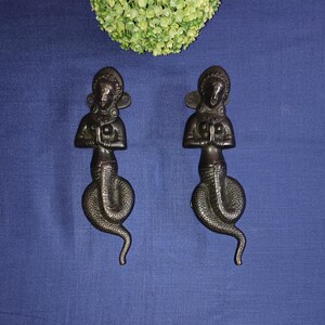 May include: Two ornate bronze door handles shaped like a woman with a snake tail. The woman is in a prayer position with her hands clasped together.