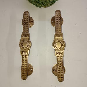 Op de afbeelding: Een paar sierlijke messing deurgrepen met een bloemmotief. De grepen zijn goudkleurig en hebben een gedetailleerd patroon.
