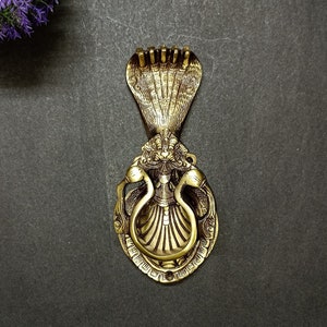 May include: A gold-toned door knocker with a detailed design of a cobra with its hood raised. The knocker is shaped like a circle with a ring in the center for knocking.