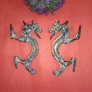 Puede incluir: Un par de tiradores de puerta de latón de estilo antiguo con forma de dragones. Los tiradores están detallados con intrincados tallados y tienen un acabado en pátina negra.