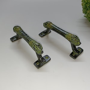 May include: Two black metal door handles with green accents. The handles have a decorative design and are shaped like a lion's head.