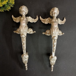 May include: Two silver-colored, decorative door handles. Each handle features a cherub with outstretched wings and a detailed, ornate design. The cherubs are attached to a long, decorative handle, perfect for adding a touch of elegance to any door.