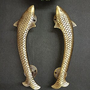 May include: A pair of gold-toned fish-shaped door handles. The handles are detailed with scales and have a curved shape.