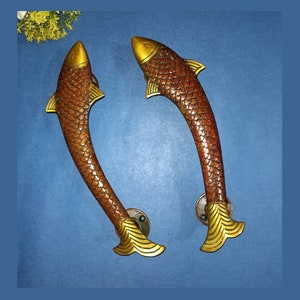 May include: Two gold-coloured fish-shaped door handles with brown scales and a gold-coloured fin. The handles are on a blue background.