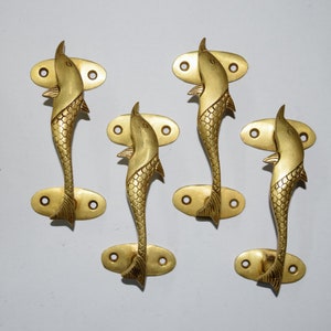Könnte beinhalten: Satz mit vier goldfarbenen Messing-Türgriffen in Form von Delfinen. Jeder Griff hat zwei Löcher zur Montage.