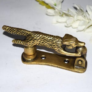 May include: A brass fox-shaped door knocker. The fox is in a leaping pose, with detailed fur texture. The knocker is mounted on a rectangular base with screw holes. The overall design is vintage and decorative.