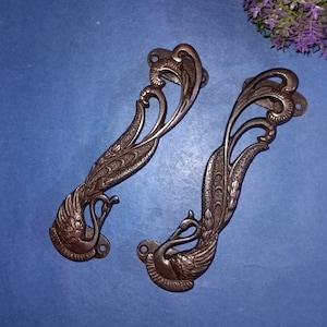 Może przedstawiać: Dwa ozdobne brązowe klamki do drzwi w kształcie pawia z misternymi detalami. Klamki są ciemnobrązowe i mają gładkie wykończenie.
