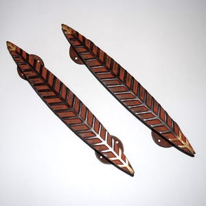 May include: Two decorative door handles in a leaf design. The handles are brown with a silver and gold leaf pattern. Each handle has a circular mounting plate with a leaf design.