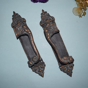May include: Two ornate brass door handles featuring an elephant design. The handles are detailed with intricate carvings and have a dark patina finish.