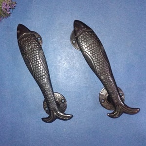 May include: Two black metal fish-shaped door handles with a detailed scale pattern. The handles have a round base with a decorative design.