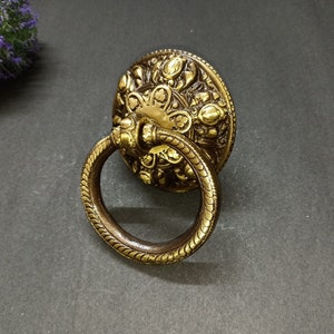 Könnte beinhalten: Ein verzierter Ringzuggriff mit einem dekorativen floralen Design. Der Griff ist aus Metall und hat eine Ringform.