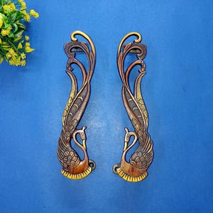 May include: Two ornate, bronze-colored door handles with a peacock design. The handles feature a swan at the base and intricate detailing throughout. The background is a solid blue.