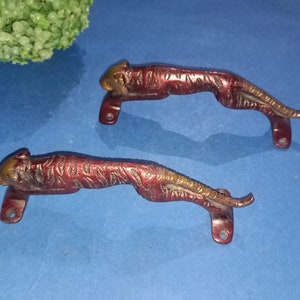 May include: Two ornate brass door handles shaped like crouching tigers. The handles are a reddish-brown colour with gold accents.