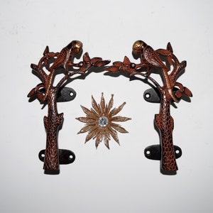 Peut inclure: Une paire de poignées de porte décoratives avec un motif de branche d'arbre et un perroquet perché sur chaque branche. Les poignées sont en métal et ont une finition brune et dorée.