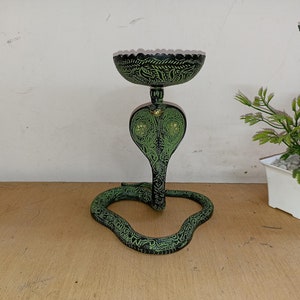 Op de afbeelding: Een zwarte en groene metalen kaarsenhouder in de vorm van een cobra met een decoratieve kom bovenop.
