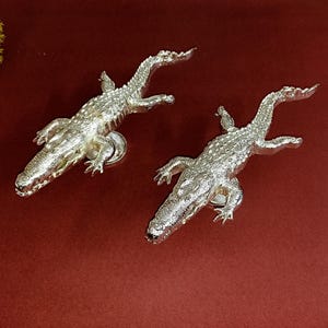 May include: Two silver alligator door handles with detailed scales and open mouths.