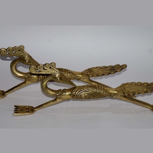 May include: A pair of gold-toned metal serving tongs shaped like peacocks with intricate details. The tongs have a fork-like design at the ends.