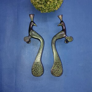 May include: A pair of peacock-shaped door handles with a green and black finish. The handles are made of metal and have a detailed design.