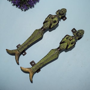 May include: A pair of decorative door handles made of brass with a green patina. The handles are shaped like women with fish tails.