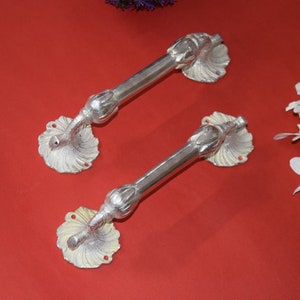 May include: Two silver door handles with a decorative floral design. The handles are made of metal and have a polished finish.